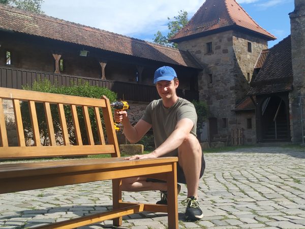 Junger Mann repariert Bank im Burghof