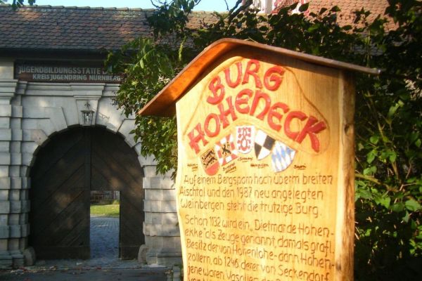 Blick auf das Burgtor mit einer hölzernen Informationstafel im Vordergrund