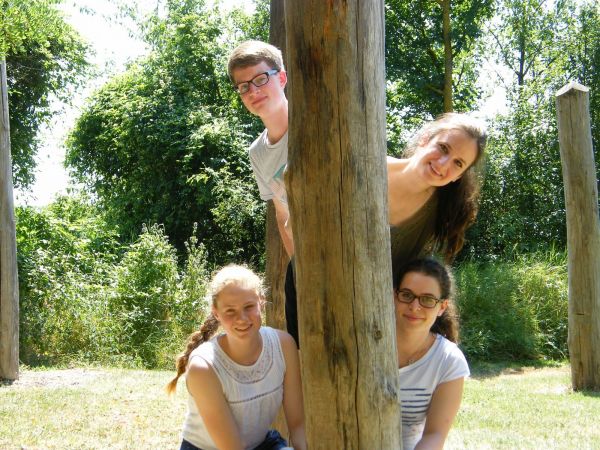 Junge Menschen schauen hinter Baumstamm hervor